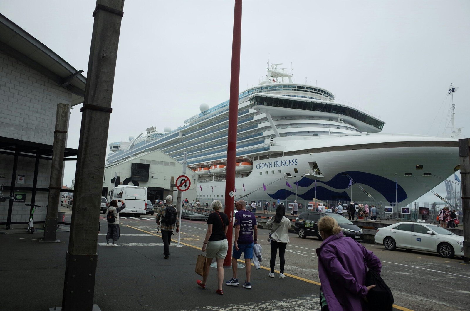 Passengers holding umbrellas at a rainy pier waiting for their tour bus