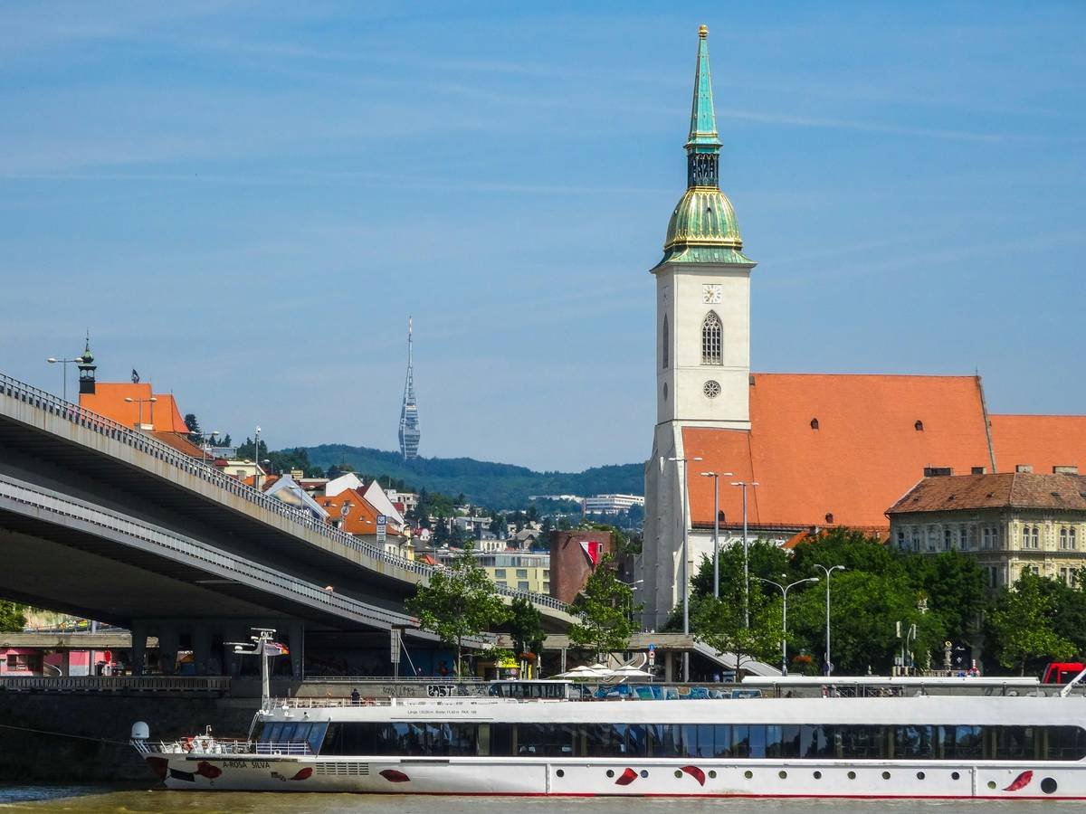 Scenic view of a luxurious river cruise ship sailing along a European river with lush greenery in the background.