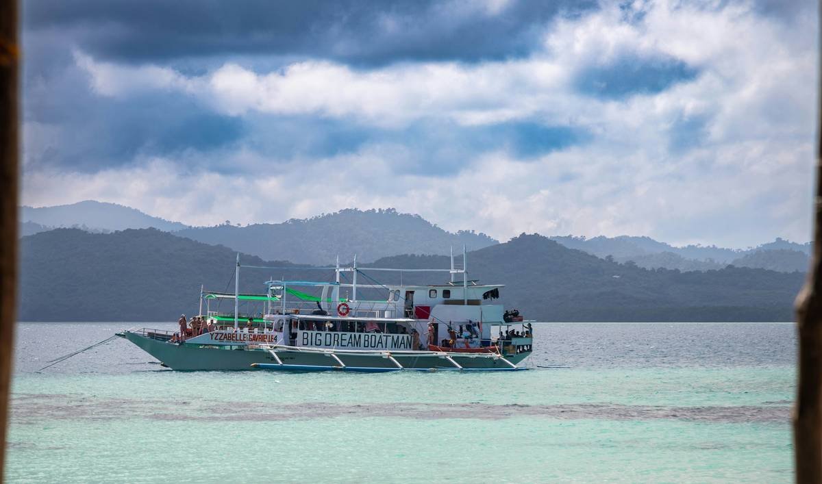 A boat floats on turquoise water near misty mountains.