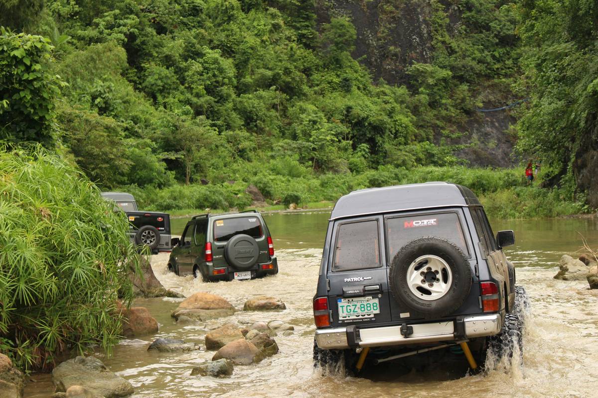 Off-road vehicles cross a shallow river.