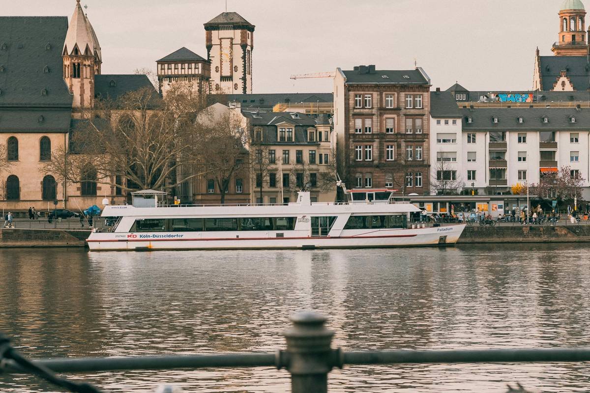 White passenger boat docked on a river with buildings behind